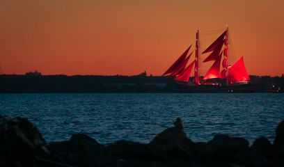 A ship with red sails at sunset on the background of a beautiful orange sky.