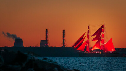 A ship with red sails at sunset on the background of a beautiful orange sky.