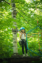 Rope adventure in the forest - a little girl standing on the stand attached to the tree