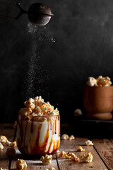 Milkshake with popcorn and caramel syrup on a black background. Sprinkle with powdered sugar.