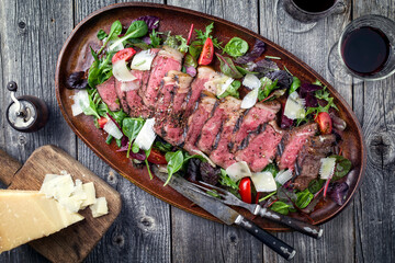 Traditional Italian tagliata steak offered with parmesan and lettuce as top view on a plate