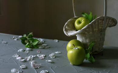 Fresh apples in and at a bamboo basket, apple tree flower petals are resting on a gray surface