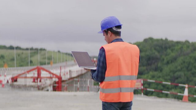 Construction engineer or an architect with a halmet and protective equipment on a building construction site using a laptop.