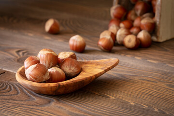 Pile of hazelnuts in a wooden olive bowl on a wooden brown table, selective focus, dark photo