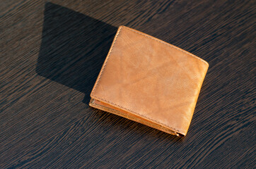 Light brown purse on a brown wooden table. The rays of the sun shine on the wallet.