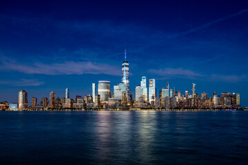 Downtown Manhattan skyline with light cirrus clouds at late blue hour as seen across the Hudson river from Exchange Place in Jersey City, New Jersey on June 21, 2020.