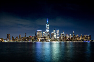 Downtown Manhattan skyline with light cirrus clouds at teal hour of the night as seen across the...