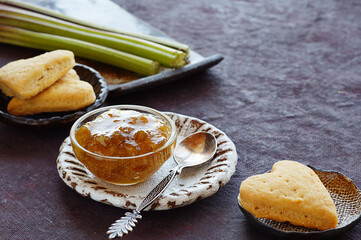 Rhubarb jam in a glass bowl on a ceramic plate with a spoon and shortbread cookies in the form of a...