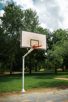 basketball court in a park with trees with white board and no net on the hoop