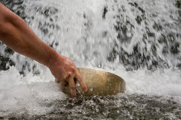 Hand picking up water with a big tibetan singing bowl from a waterfall.