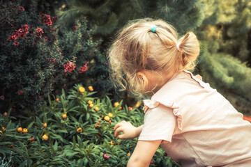 Child girl smelling beautiful flowers in blossoming summer park concept saving nature lifestyle