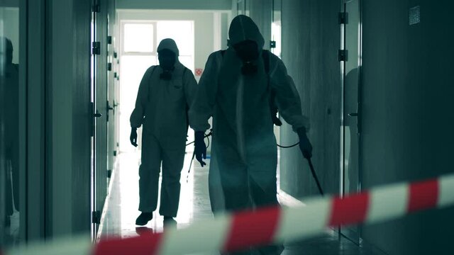 Male disinfectors work in restricted area, spraying.