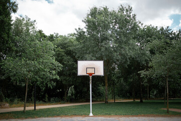 basketball court in a park with trees with white board and no net on the hoop - 360038492