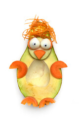 Food art creative concept. Funny penguin made of avocado, cucumber and carrots over white background. Creative fun healthy food concept, an avocado cut in half with funny googly eyes.