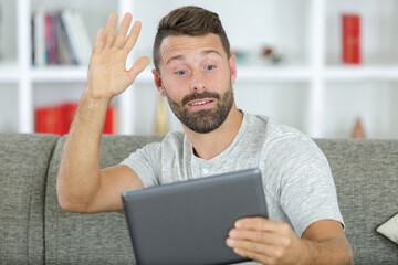 smiling young man waving at digital tablet