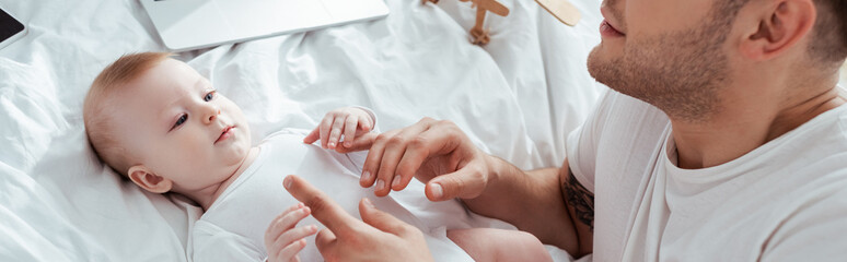 cropped view of young father touching hands of adorable infant, horizontal image
