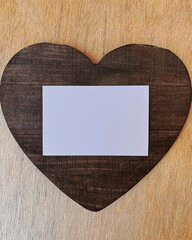 on the table lies a wooden dark brown heart-shaped board on top of it is an empty white card with free space for text or inscription, the background for the design of postcards, copy space