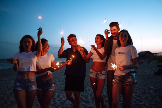 Group of young people having fun with sparklers outdoors at the sea shore. People celebrating new year's day at the beach. Beach party, rest, vacation.