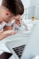 Obraz premium selective focus of young father lying on bed near adorable little son and gadgets