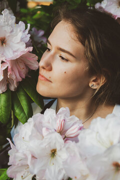 A close up of a person holding a flower. High quality photo. Portrait of young lady in flower bush and she is looking on left side. Botanical garden photo with white flowers and lady.