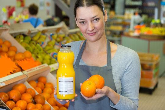 Female Grocer Holding Oranges And Bottle Of Juice