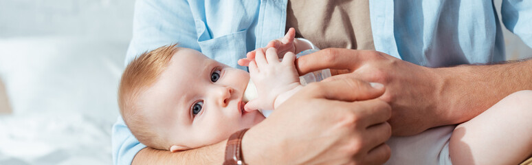 partial view of father feeding son with milk from baby bottle, horizontal image