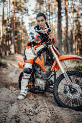 Fototapeta na wymiar Beautiful young brunette female racer riding motocross bike on a trail of sand in the woods