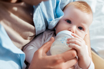 cropped view of father feeding son with milk from baby bottle