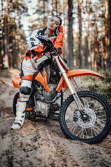 Beautiful young brunette female racer riding motocross bike on a trail of sand in the woods