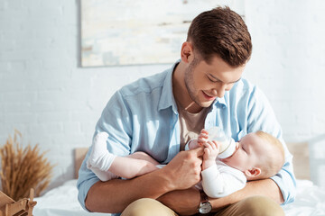 happy young father feeding cute baby boy with milk from baby bottle - Powered by Adobe