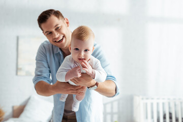 cute baby boy looking at camera on hands of happy father
