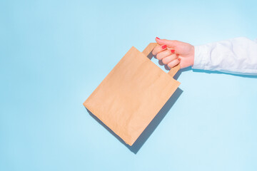 hand holding shopping paper bag. Concept of consumerism, shopping symbol. Copy space trend pastel color. Hard shadows, morning light.