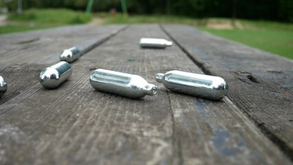 Multiple metallic nitrous oxide gas cylinder recreational drug slow motion on wooden park table dolly left