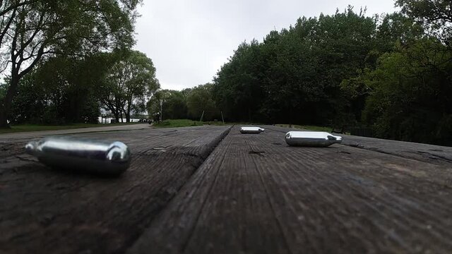 Multiple metallic nitrous oxide gas cylinder recreational drug slow motion falling onto wooden table bench