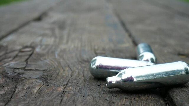 Multiple metallic nitrous oxide gas cylinder recreational drug slow motion on wooden park table