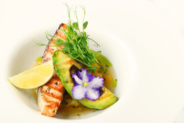 plate of grilled salmon steak with avocado and microgreen closeup