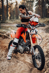 Beautiful female racer wearing motocross outfit with semi naked torso sitting on her bike in the forest