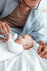 young father feeding adorable son from baby bottle on bed