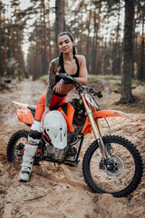 Fototapeta na wymiar Charming young female racer with semi naked torso sitting on her bike in the woods, smiling and lokking on the camera
