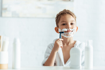 selective focus of cute boy shaving in bathroom near toiletries
