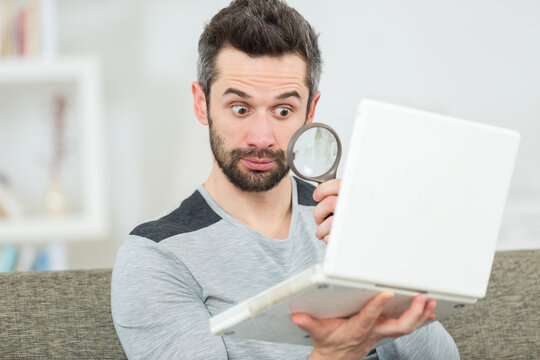 handsome man looking at his laptop through manifying glass