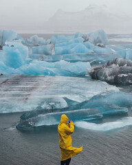 Man on a background of large blue icebergs in the Arctic. Traveler in a yellow raincoat on the background of a glacier in Iceland. Epic landscape with a man. Travel and adventure concept.