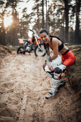Fototapeta premium Beautiful brunette girl wearing motocross outfit with semi naked torso sitting on grass and unrestrained laughs