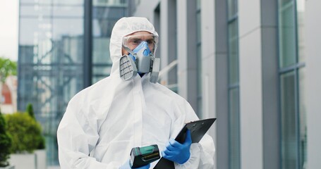 Female office worker in mask going to work and man in white suit and respirator measuring her...