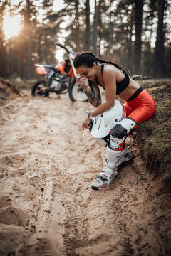 Beautiful brunette girl wearing motocross outfit with semi naked torso sitting on grass and unrestrained laughs