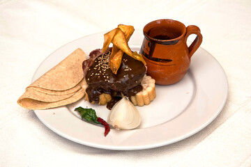 Plato de mole de olla acompañado de tortillas, elote, plátano frito y jarrito de barro, comida mexicana