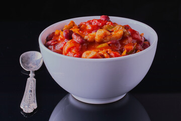 Bowl of Mexican chilli, shot on a black surface, with a black background.