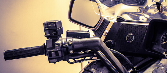 The left side of motorcycle steering wheel closeup. Moto handle, control block,clutch lever, windshield, mirror, speaker, speedometer. Photo in vintage style of large motorbike. Banner for web site