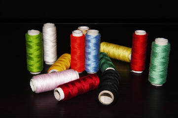 Rolls of colored cotton threads for hand and machine stitching.Isolated on black background and arranged unevenly.