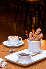 churros con chocolate para remojar y café capuchino sobre mesa de madera en restaurante	